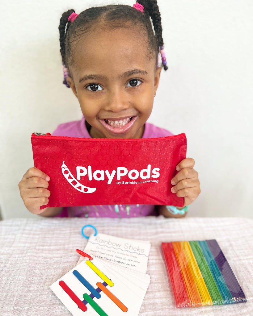 Smiling girl holding red PlayPod with contents on table