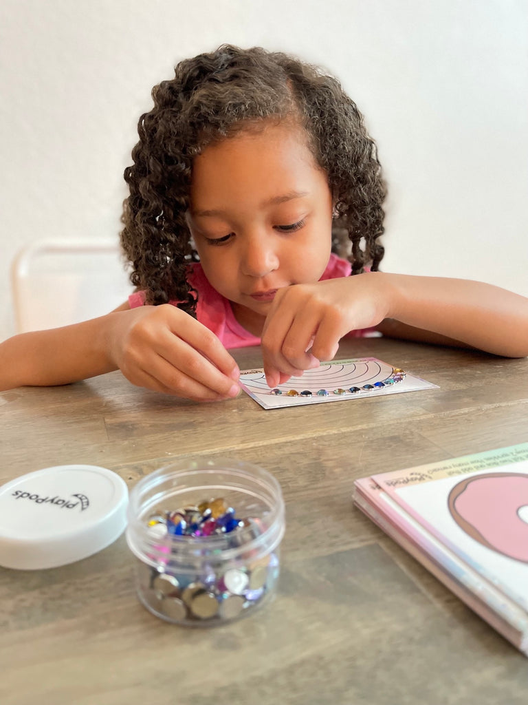 Little girl putting colorful gems on a rainbow activity card