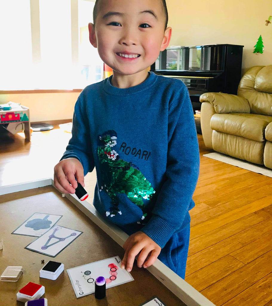 Smiling boy in dinosaur shirt playing with stamps
