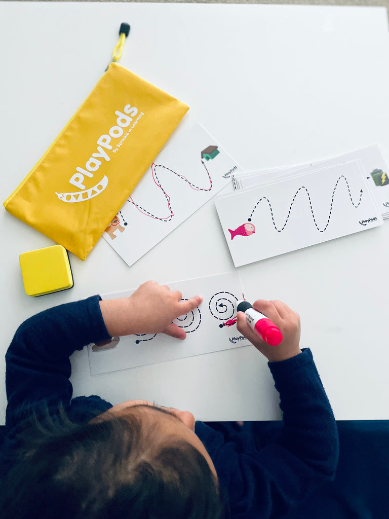 Child following lines on a write and wipe card with yellow play pod on the table