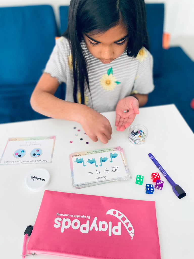 Girl at table with pink PlayPod, activity cards, colorful dice, and gems