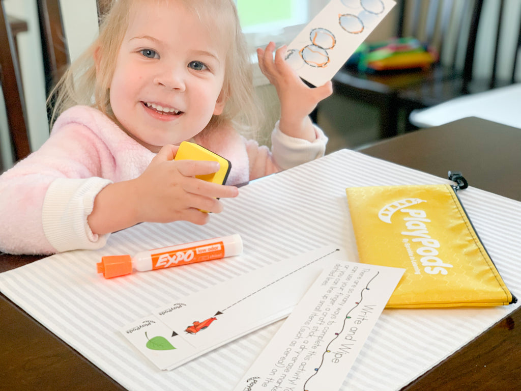 Smiling little girl holding up a card she traced with an orange marker