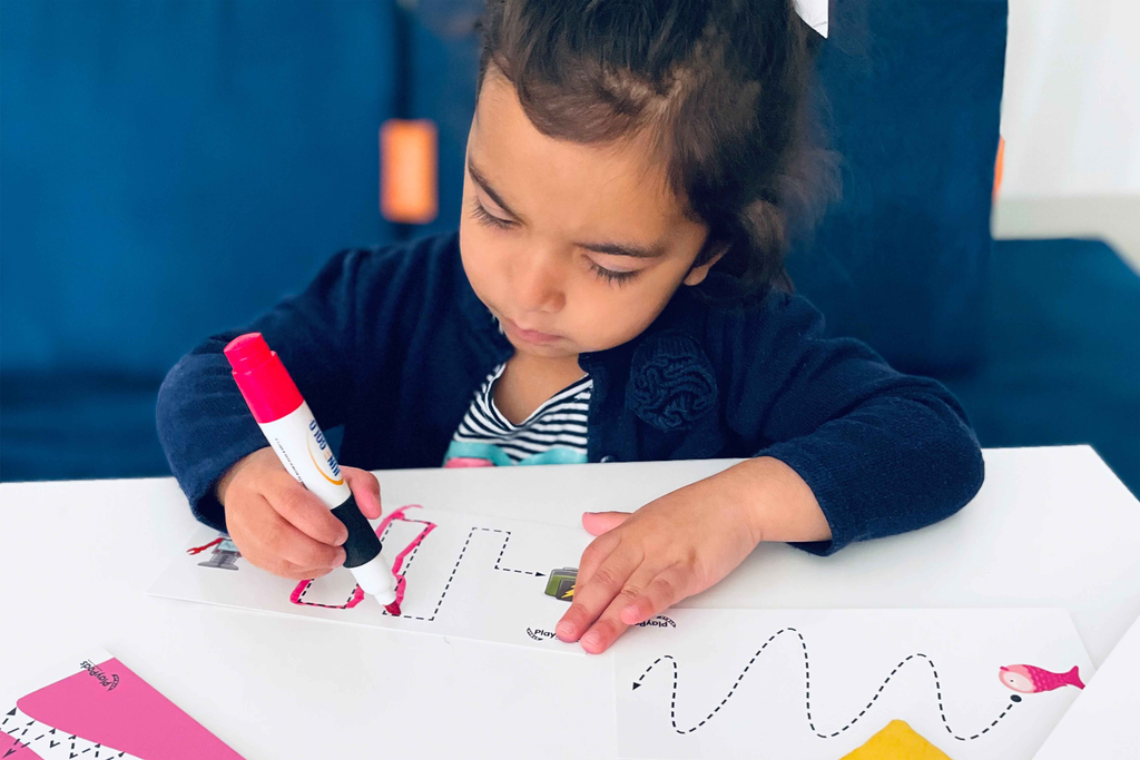 Little girl using a red marker to trace lines on a write and wipe card