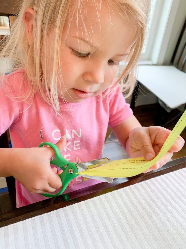 Little girl in pink shirt cutting yellow paper with green scissors