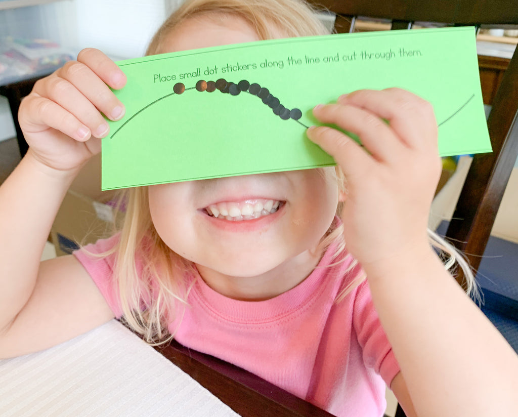 Smiling little girl holding green paper with stickers  over her eyes