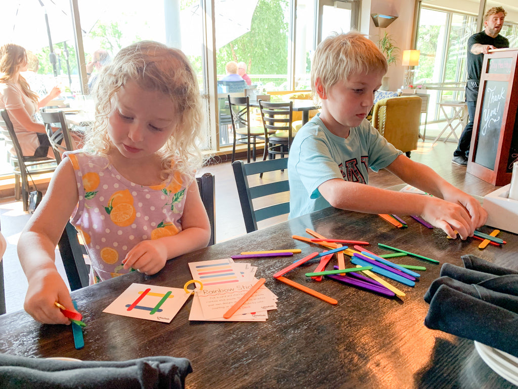 Little girl and boy playing with colorful popsicle sticks at a restaurant